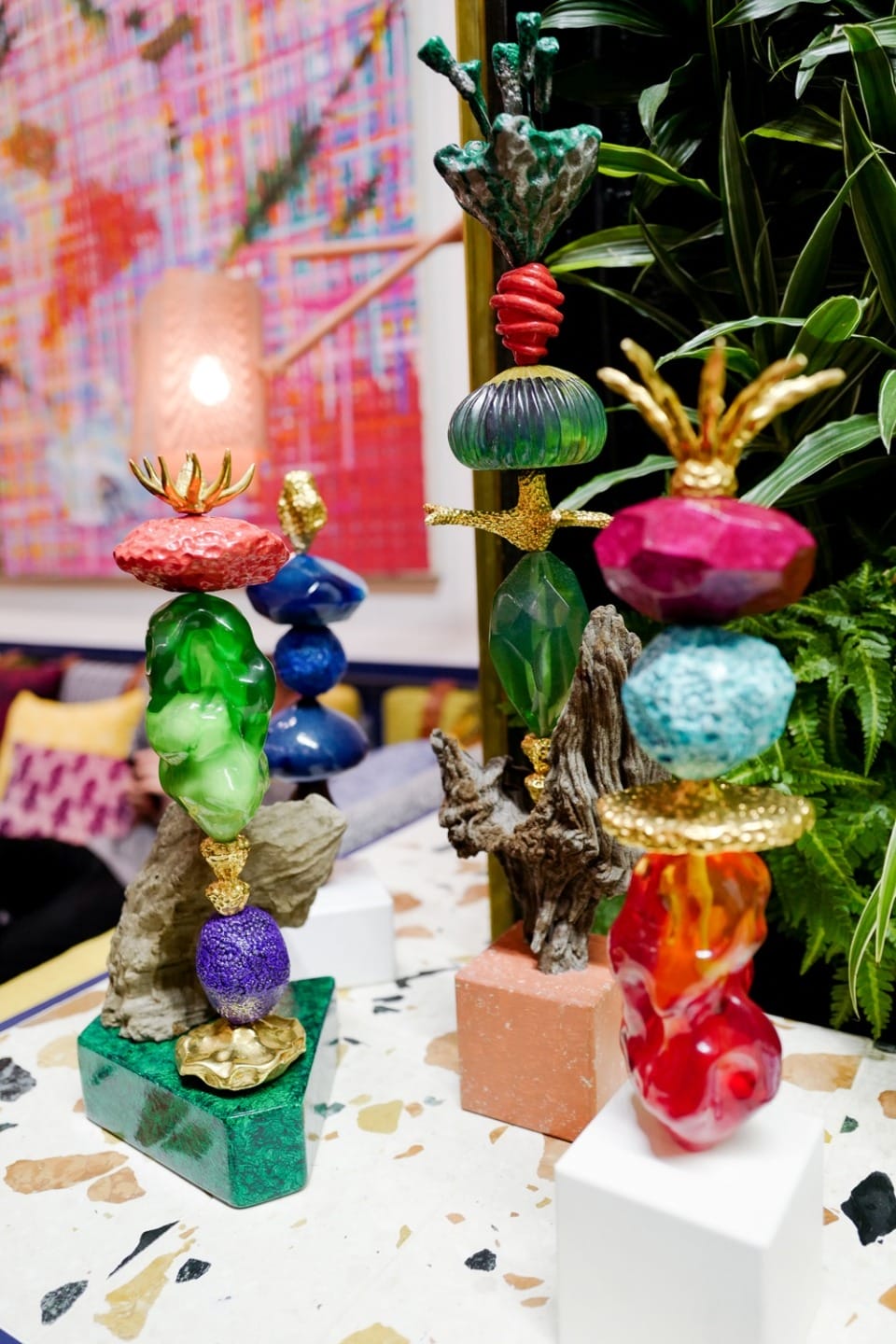 Colorful, abstract sculptures displayed on a patterned marble surface with a vibrant, colorful background.