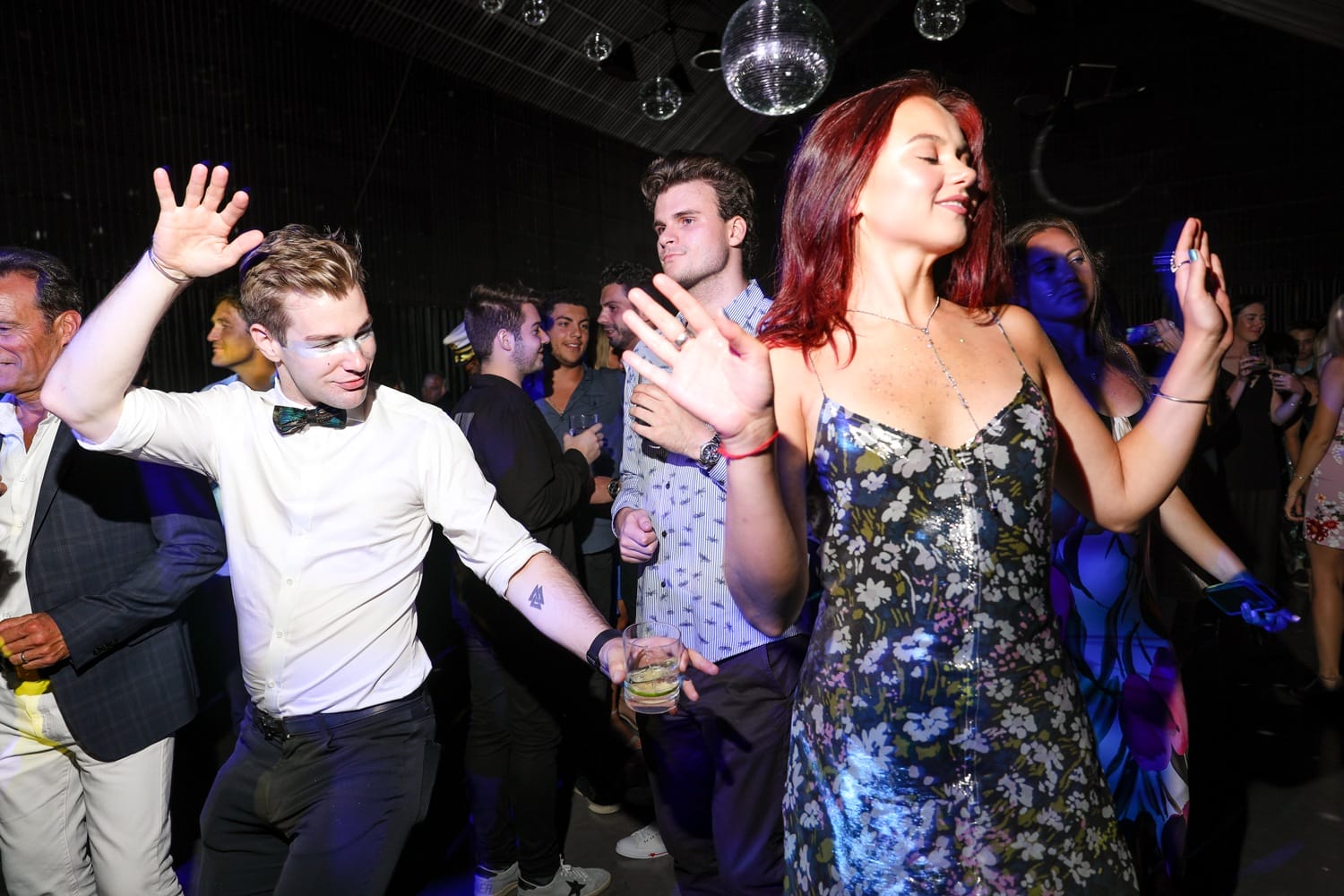 People dancing energetically at a lively party with disco balls overhead.