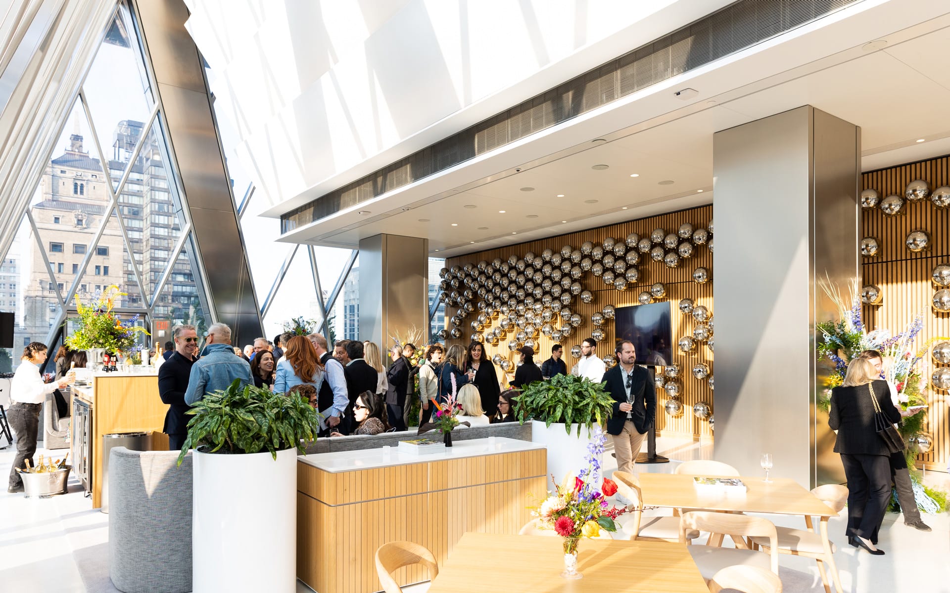 People mingling at a modern indoor event space with plants, wooden decor, and reflective wall art.