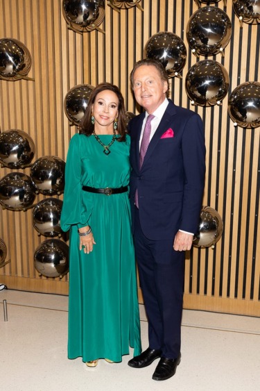 Elegant couple posing in formal attire next to a modern wall with reflective metallic spheres.