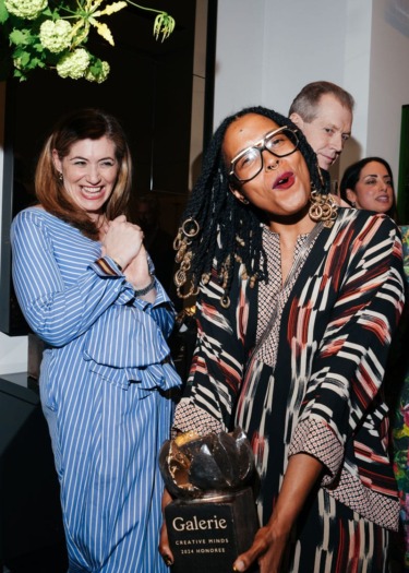 Two people smiling at an event, one holding a "Galerie Creative Minds 2023 Honoree" award, surrounded by others.