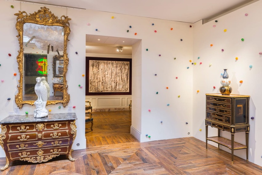 Elegant room with ornate mirror, marble-topped dresser, colorful wall decor, and parquet floor in artistic setting.