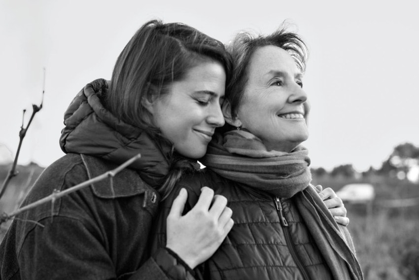 Two women smiling and embracing outdoors, enjoying a serene moment together in a black and white photo.