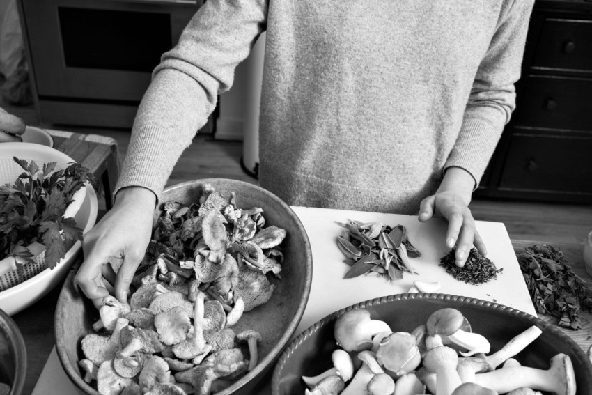 Person preparing mushrooms and herbs in a kitchen setting with various ingredients on the table.