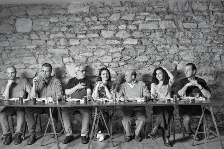 Group of seven people sitting at a long table against a stone wall.