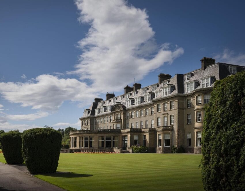 Large historic building with manicured lawn and topiary under a blue sky with clouds.