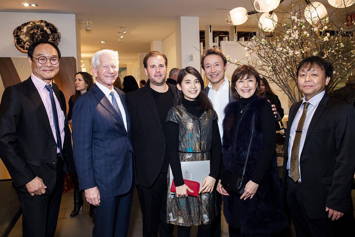 Group of seven people posing for a photo at an indoor event, with a decorated background and modern lighting.