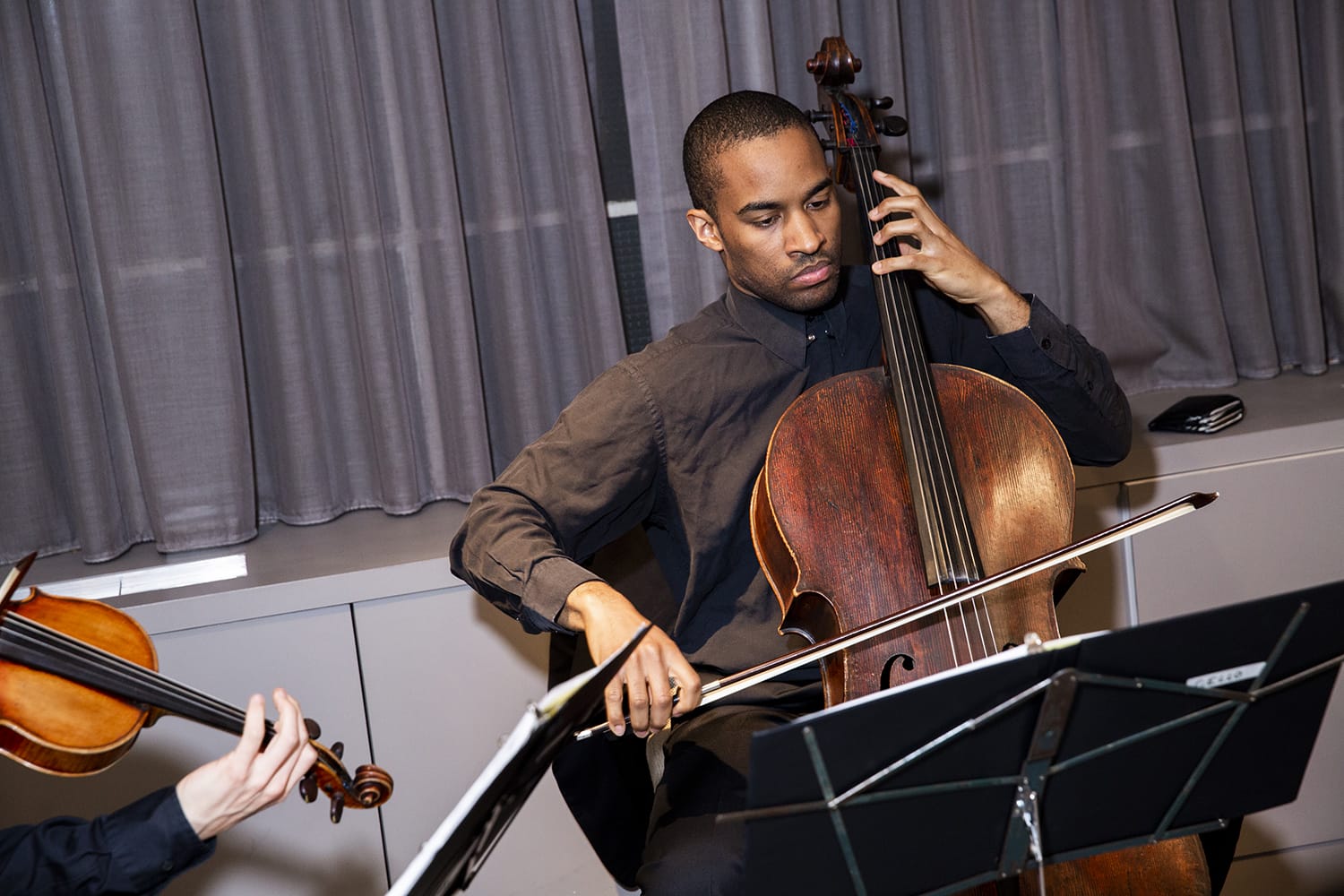 Musician playing the cello with focused expression alongside violinist in performance setting
