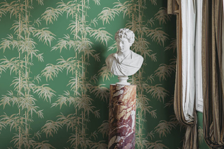 Bust on a marble pedestal by a window, set against a green wallpaper with a bamboo pattern.