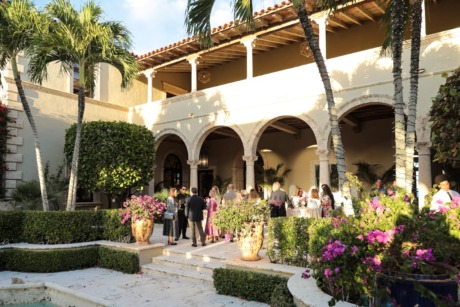 Elegant outdoor gathering at a luxurious villa with tropical greenery, arched architecture, and guests enjoying an event.