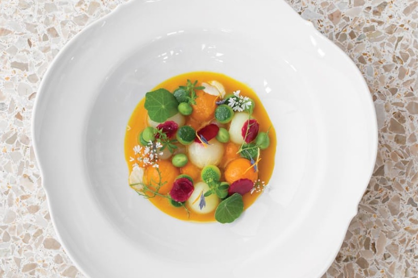 Gourmet salad with colorful vegetables and edible flowers in a white bowl on a textured stone-like surface