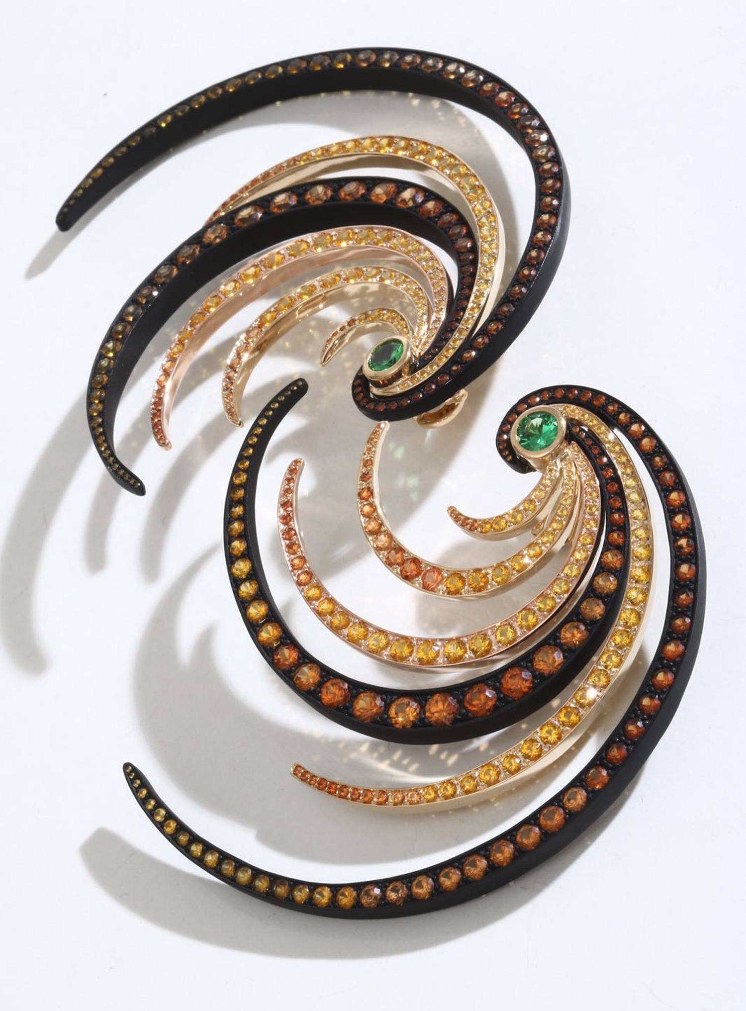 Colorful spiral earrings with gemstones in amber and green tones on a white background, resembling abstract art.