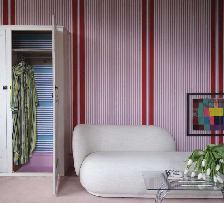 Modern interior with a white sofa, striped walls, open wardrobe, striped dress, glass table, and vase of white tulips.