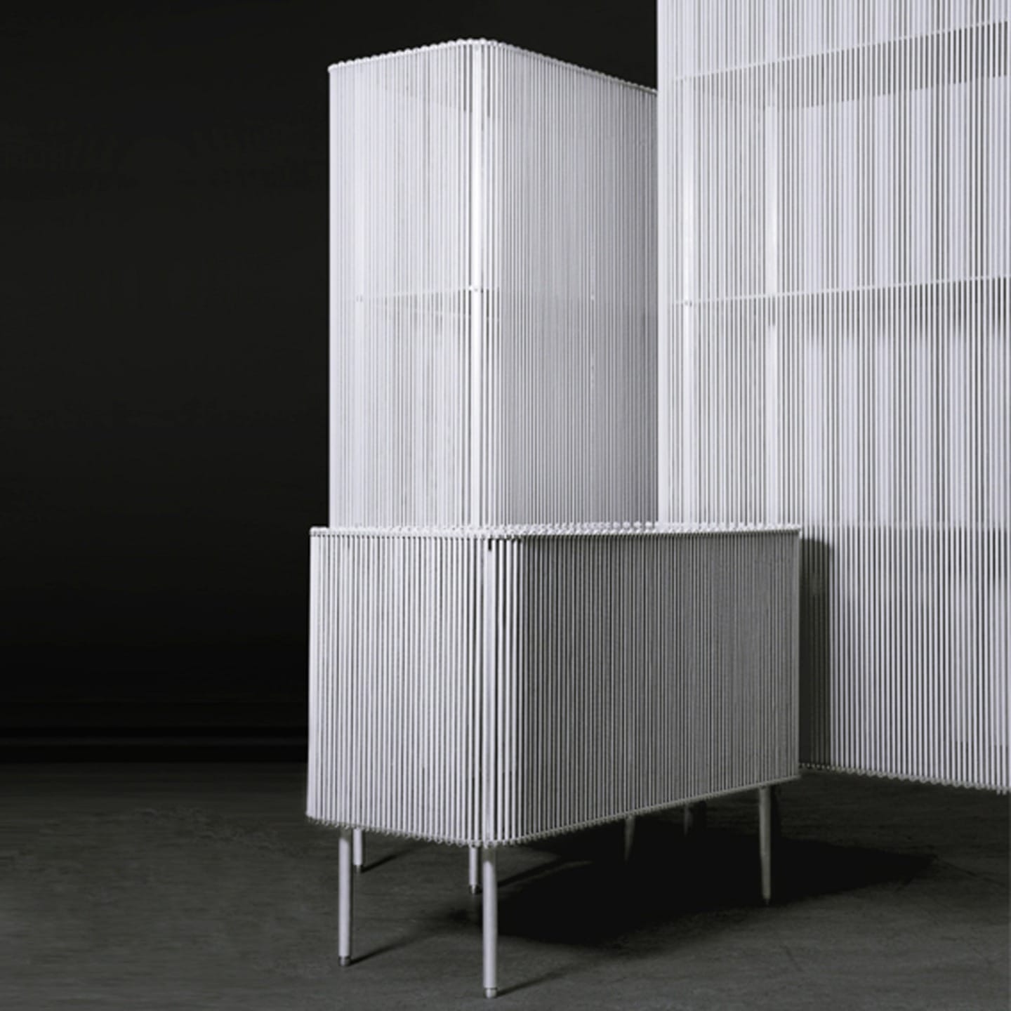 Modern white minimalist cabinet with vertical slats against a dark background.