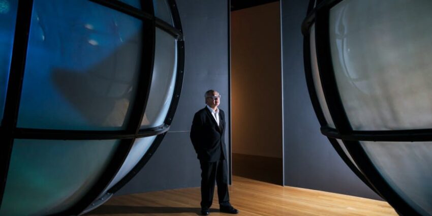 Person in a suit standing between two large spherical structures in a modern, dimly lit environment.