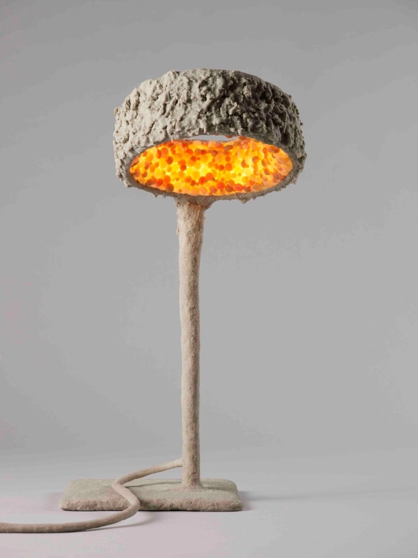 Textured lamp with a rough stone-like exterior and warm glowing interior, standing on a cylindrical base with a visible cord.