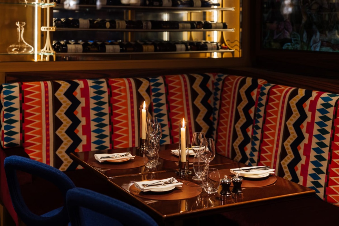 Cozy restaurant booth with colorful patterned cushions, set with plates, glasses, and lit candles.