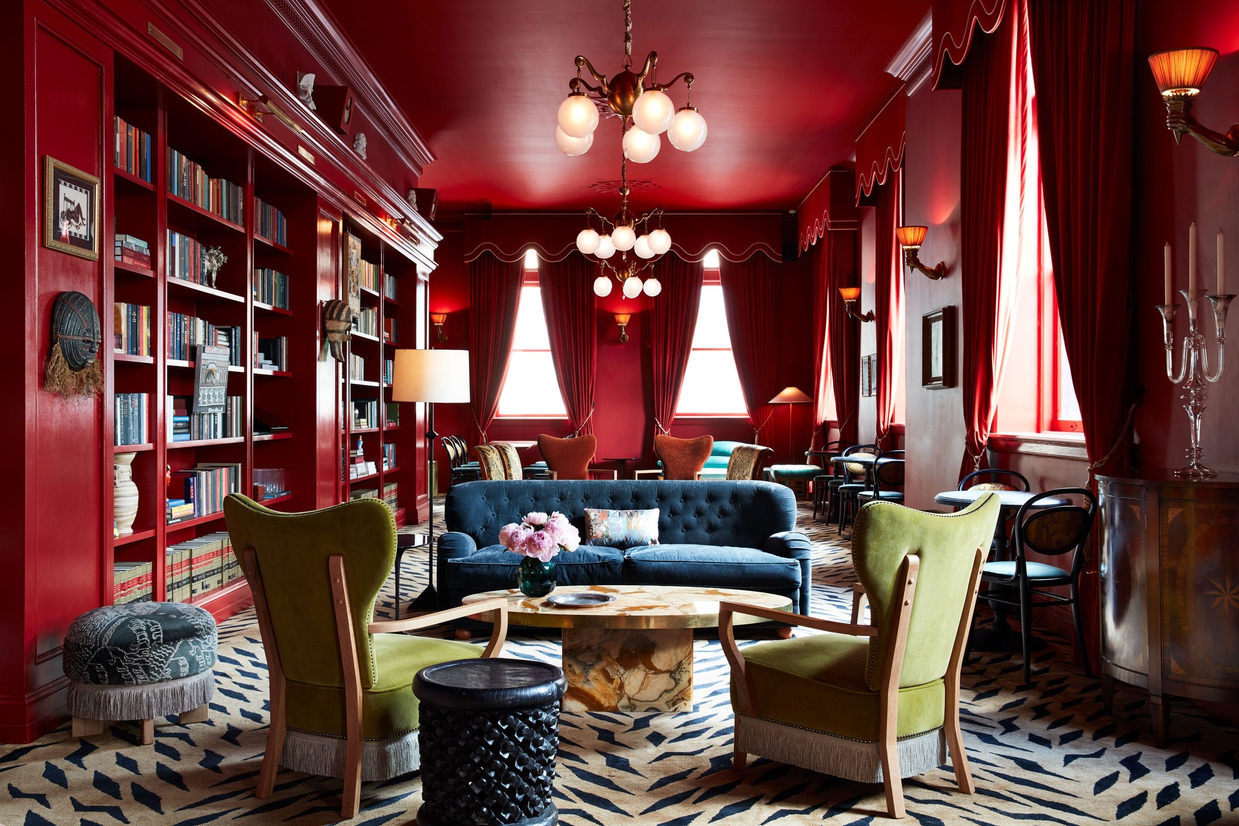 Luxurious red lounge with elegant furniture, bookshelves, and decorative lighting creating a sophisticated ambiance.
