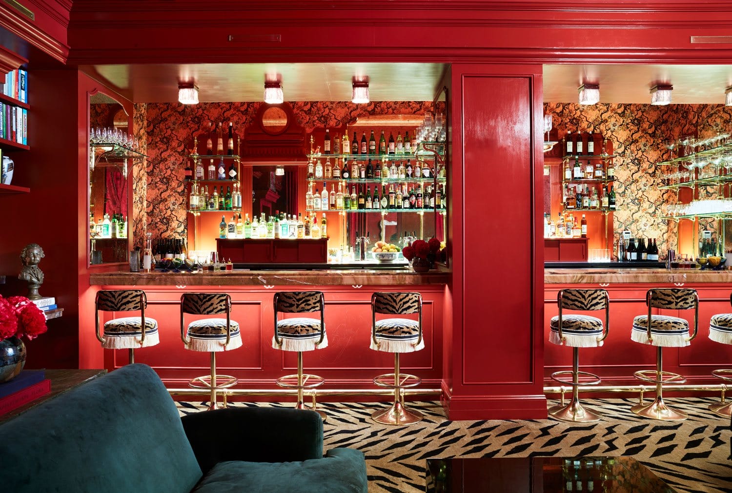 Luxurious red-themed bar interior with patterned stools, fully stocked shelves, and elegant lighting.