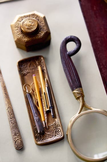 Elegant vintage desk set with magnifying glass, pens, pencils, and ornate hexagonal container on light background