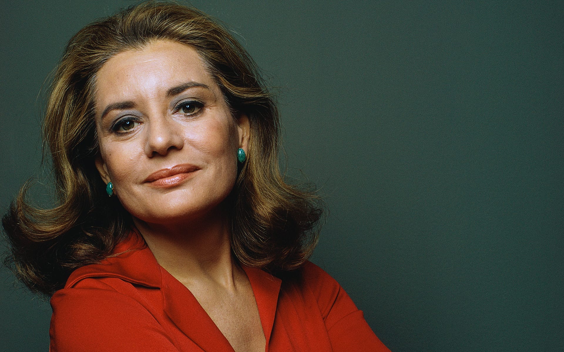Person with brown hair and a red blouse, looking confidently at the camera against a green background.