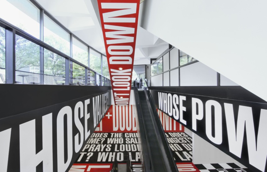 Escalator surrounded by bold black and red text art in a modern architectural space, viewed from above.