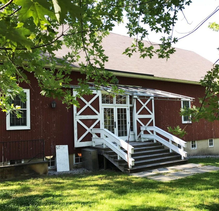 red barn with white trim and steps surrounded by trees and green grass on a sunny day