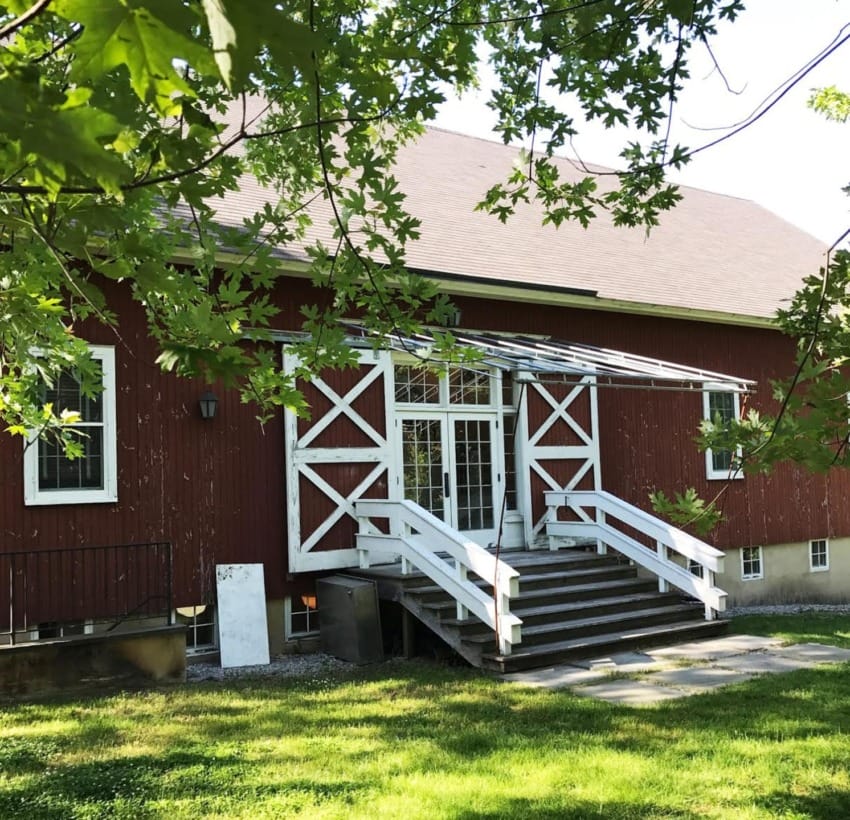 red barn with white trim and steps surrounded by trees and green grass on a sunny day