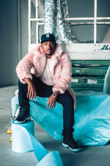 Man in pink fur coat and cap sitting on construction equipment with blue fabric around.