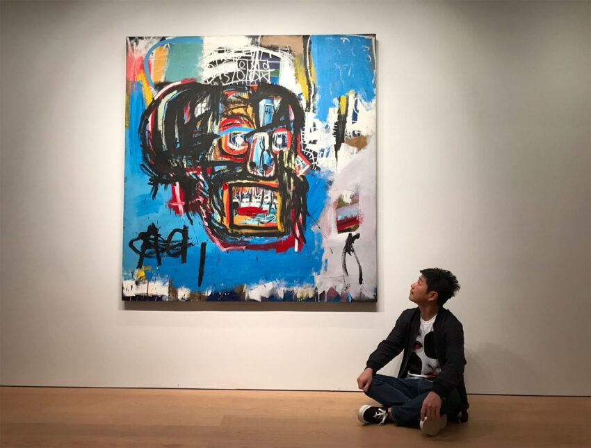 Person sitting on the floor in a gallery, looking at a large, colorful abstract painting on the wall.