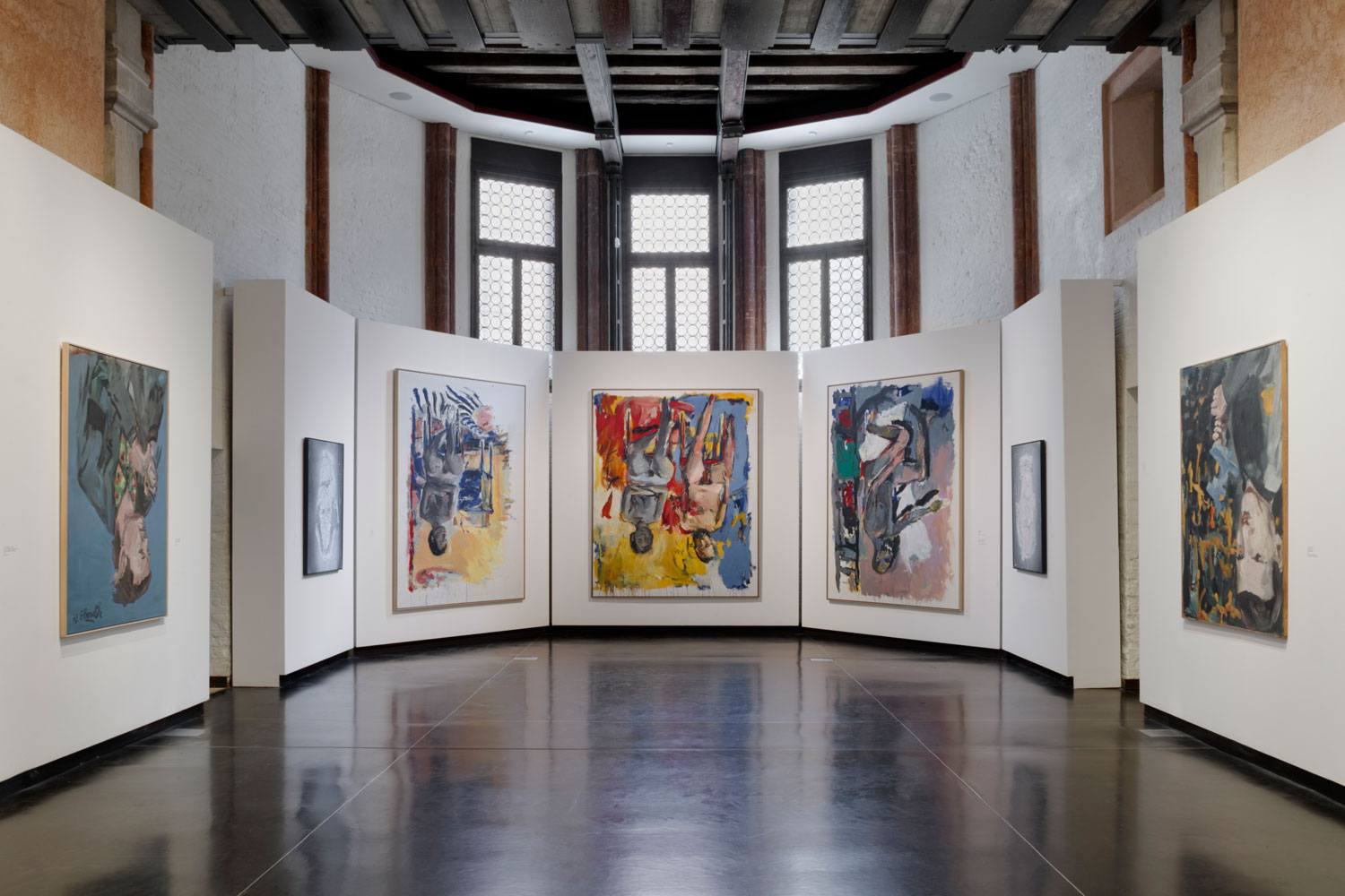 Contemporary art gallery with large colorful paintings displayed on curved white walls under a high ceiling.