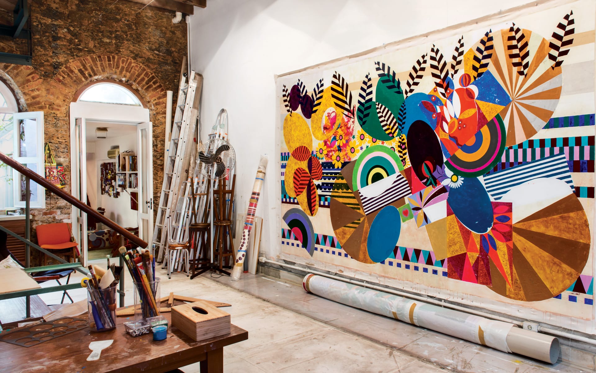 Colorful abstract mural in art studio with bright patterns and shapes, surrounded by ladders and art supplies.