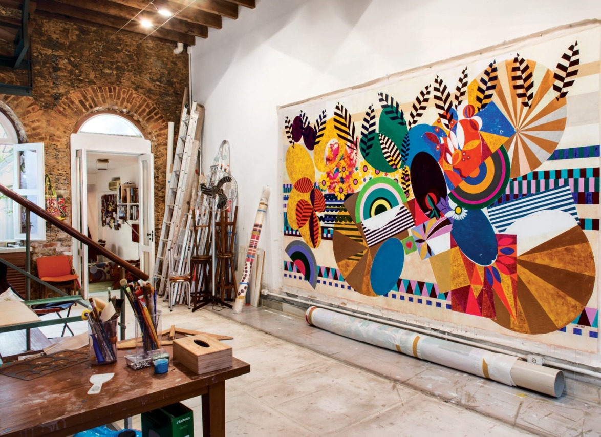 Artistic studio with a vibrant abstract mural in progress, surrounded by art supplies, ladders, and exposed brick walls.