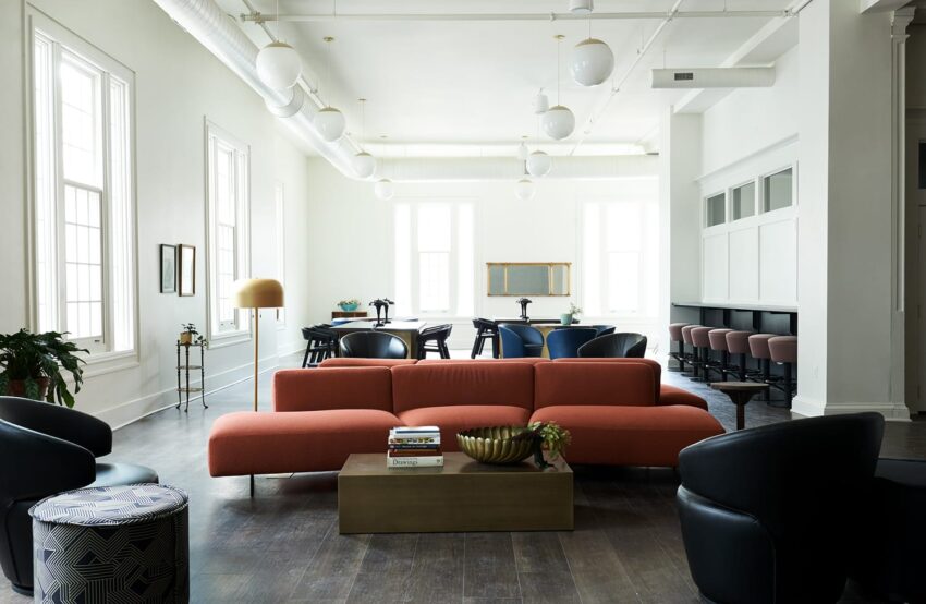 Modern open-plan room with a long orange sofa, dark chairs, a wooden table, and spherical pendant lights.