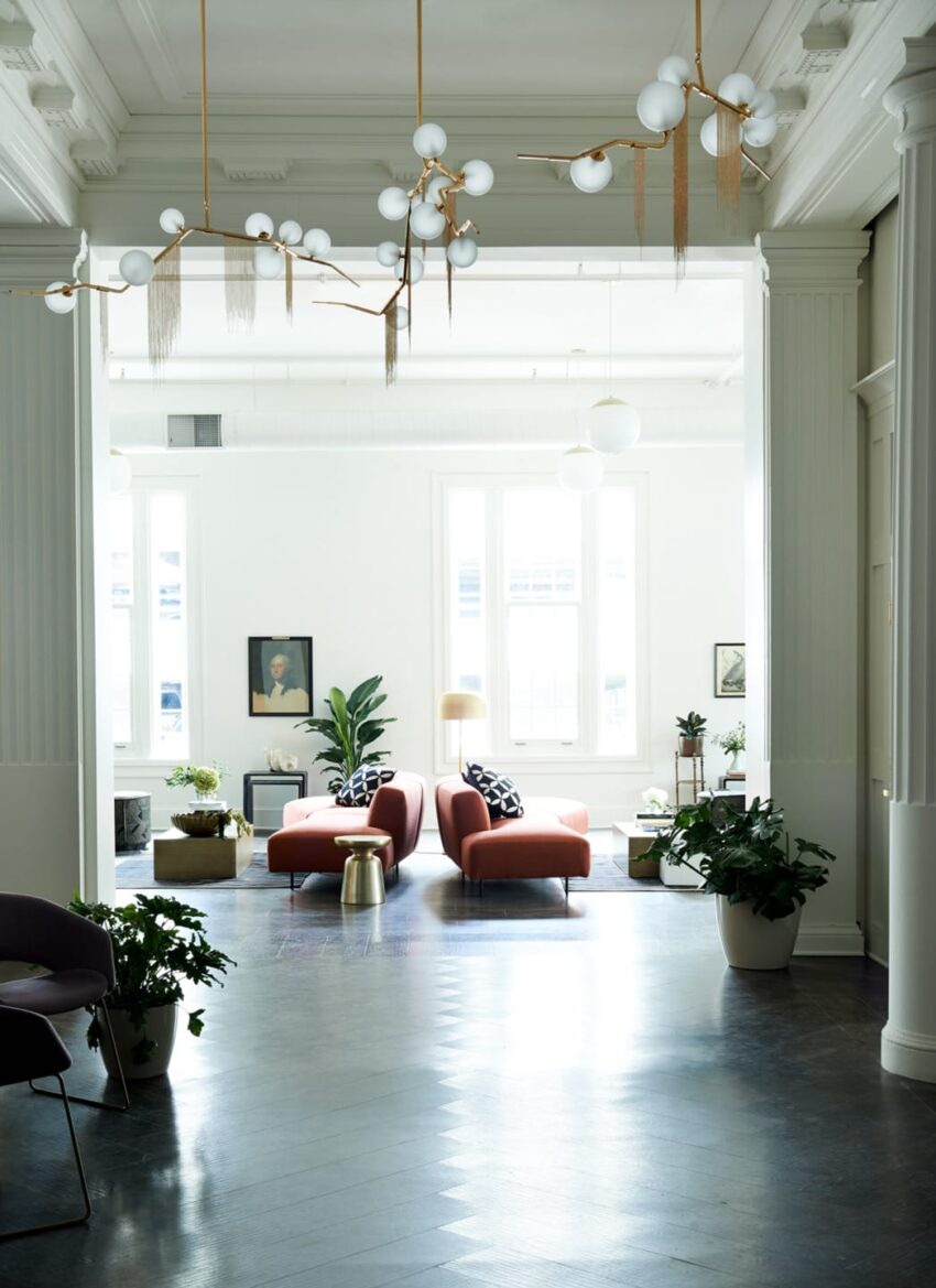 Spacious modern living room with red sofas, plants, and elegant light fixtures under natural light.