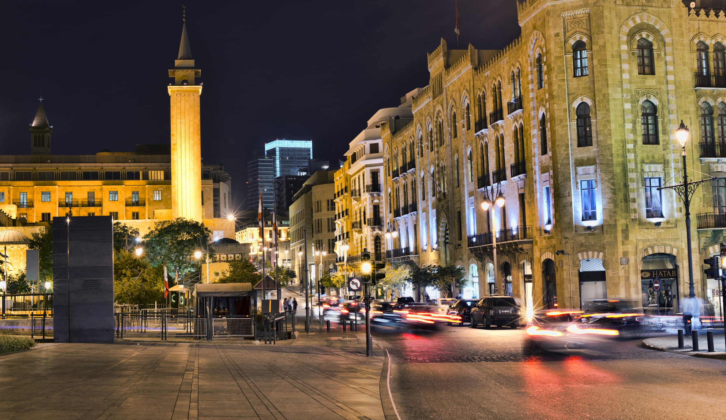 Downtown cityscape at night with illuminated historic buildings and a mosque, cars moving on the street in the foreground.