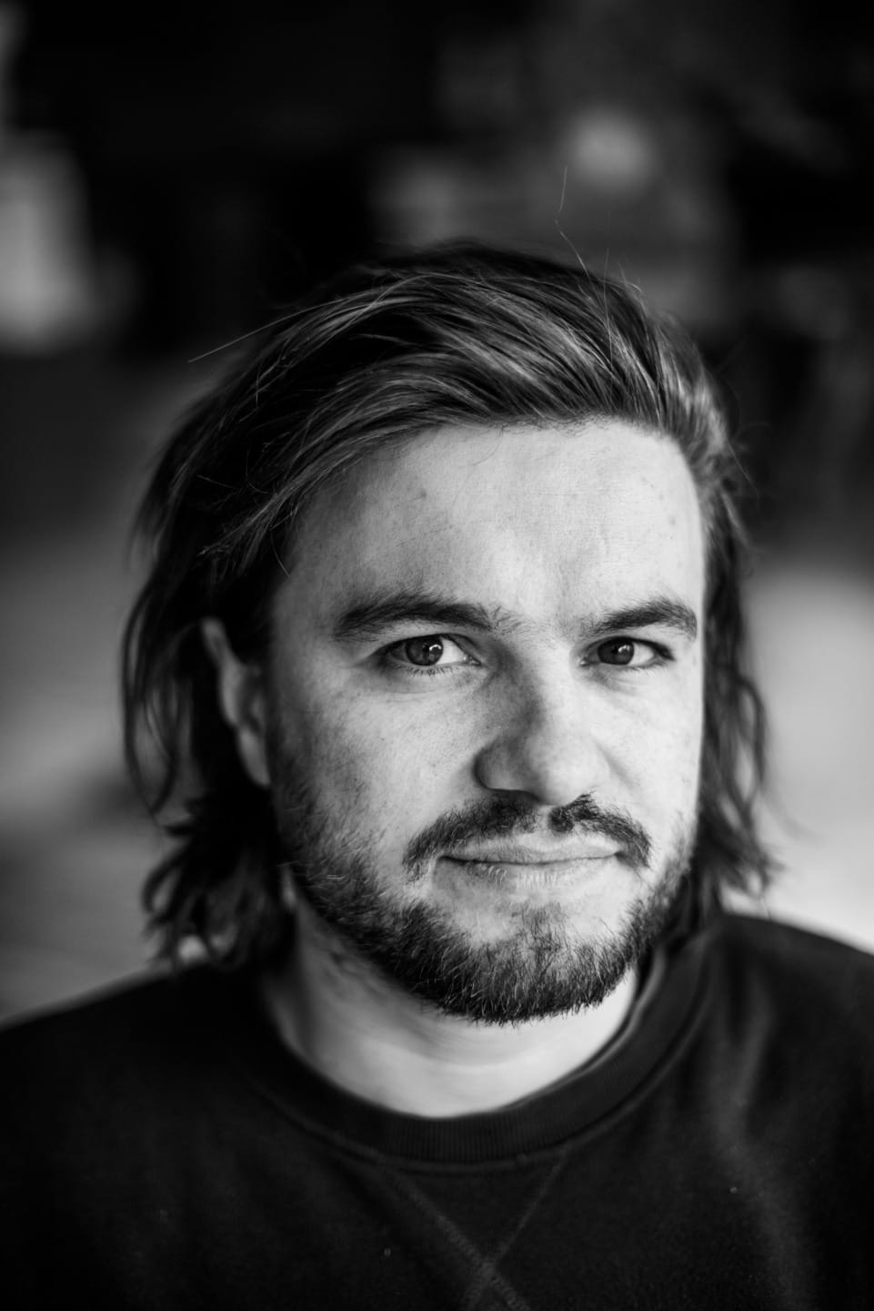Person with medium-length hair and beard, looking directly at the camera, in a black and white portrait.