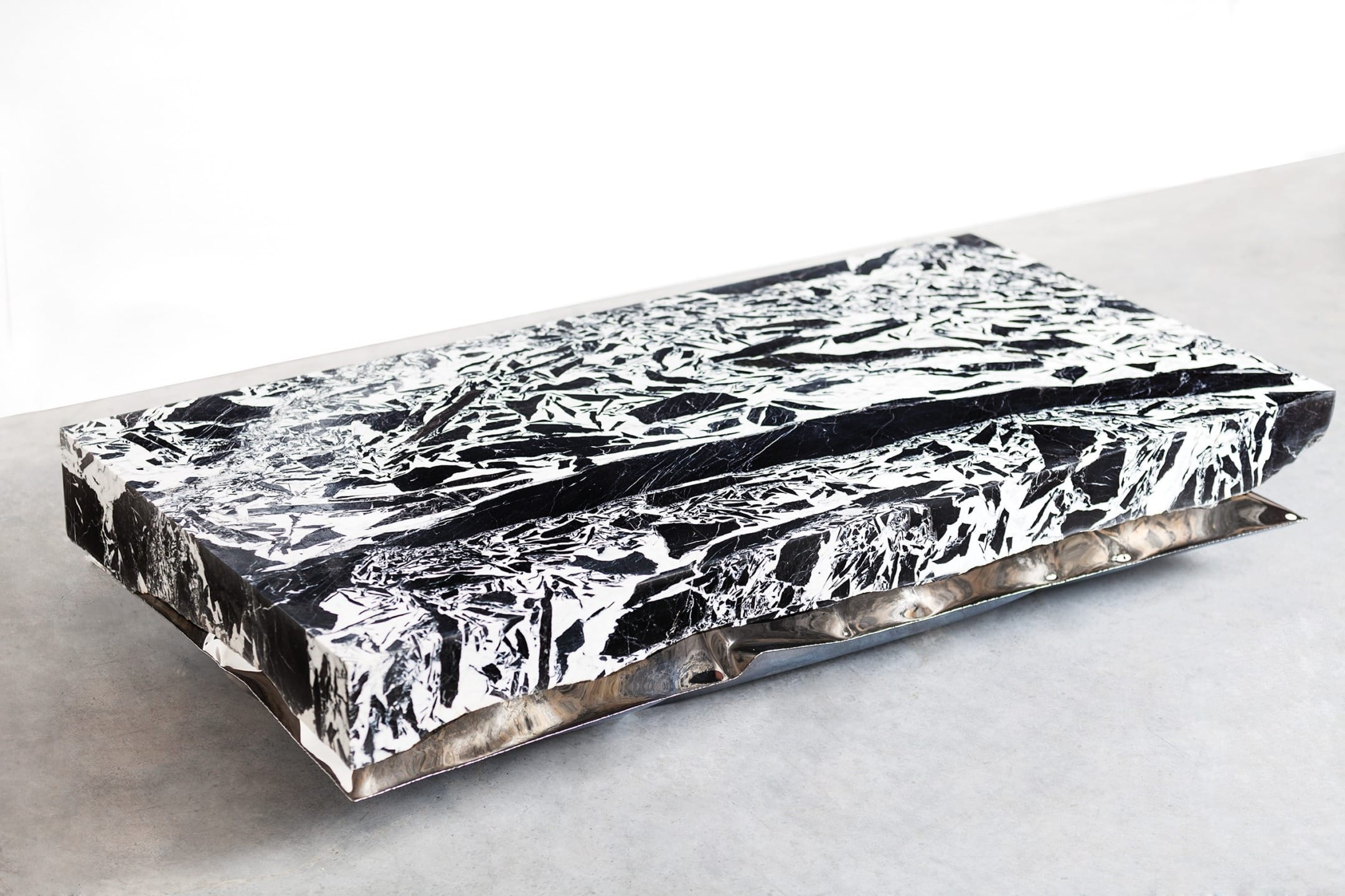 Rectangular abstract coffee table with a black and white crumpled paper design on a concrete floor.