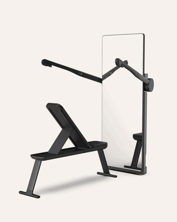 Home gym setup with mirror, adjustable bench, and extendable arms against a neutral background.
