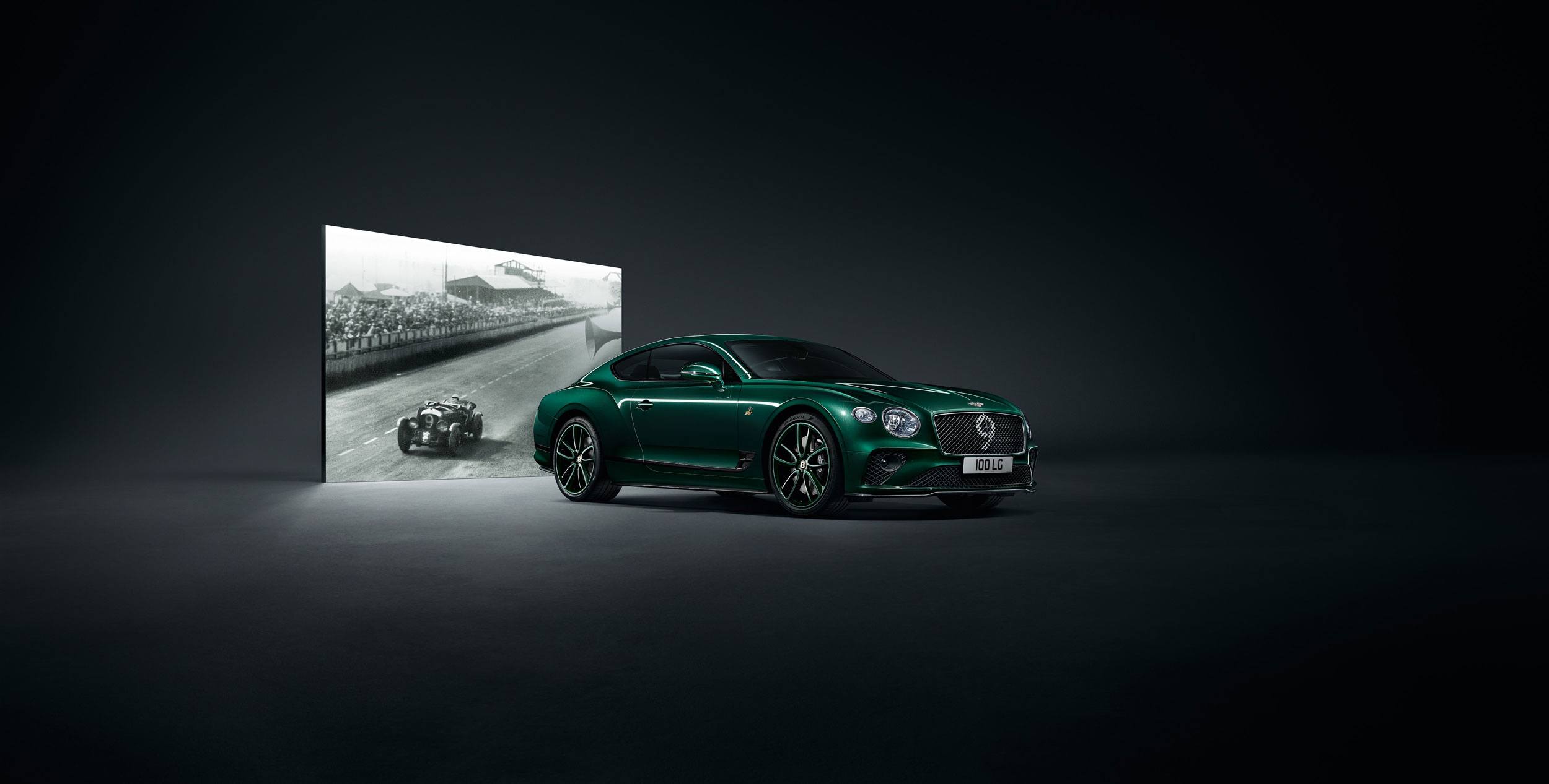 Green luxury car parked in dark setting with vintage racing scene projected in the background.