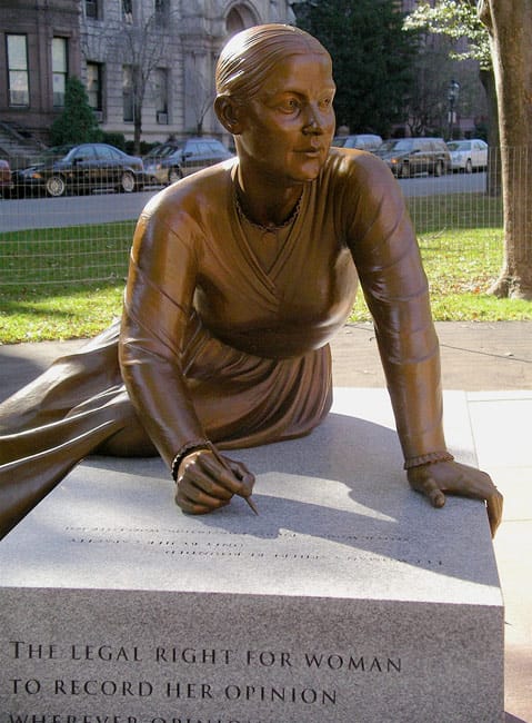 Statue of a woman writing on a stone, symbolizing women's rights and the importance of recording opinions.
