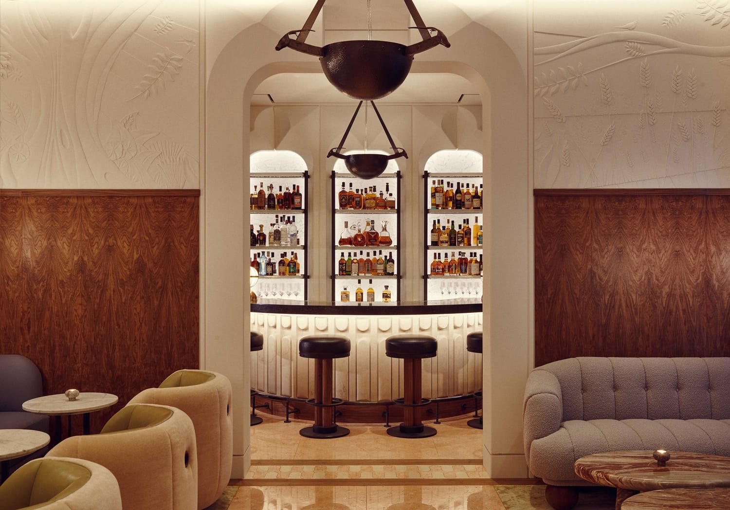 Elegant bar interior with archway, backlit shelves of bottles, stools at the counter, and cozy seating with wood paneling.