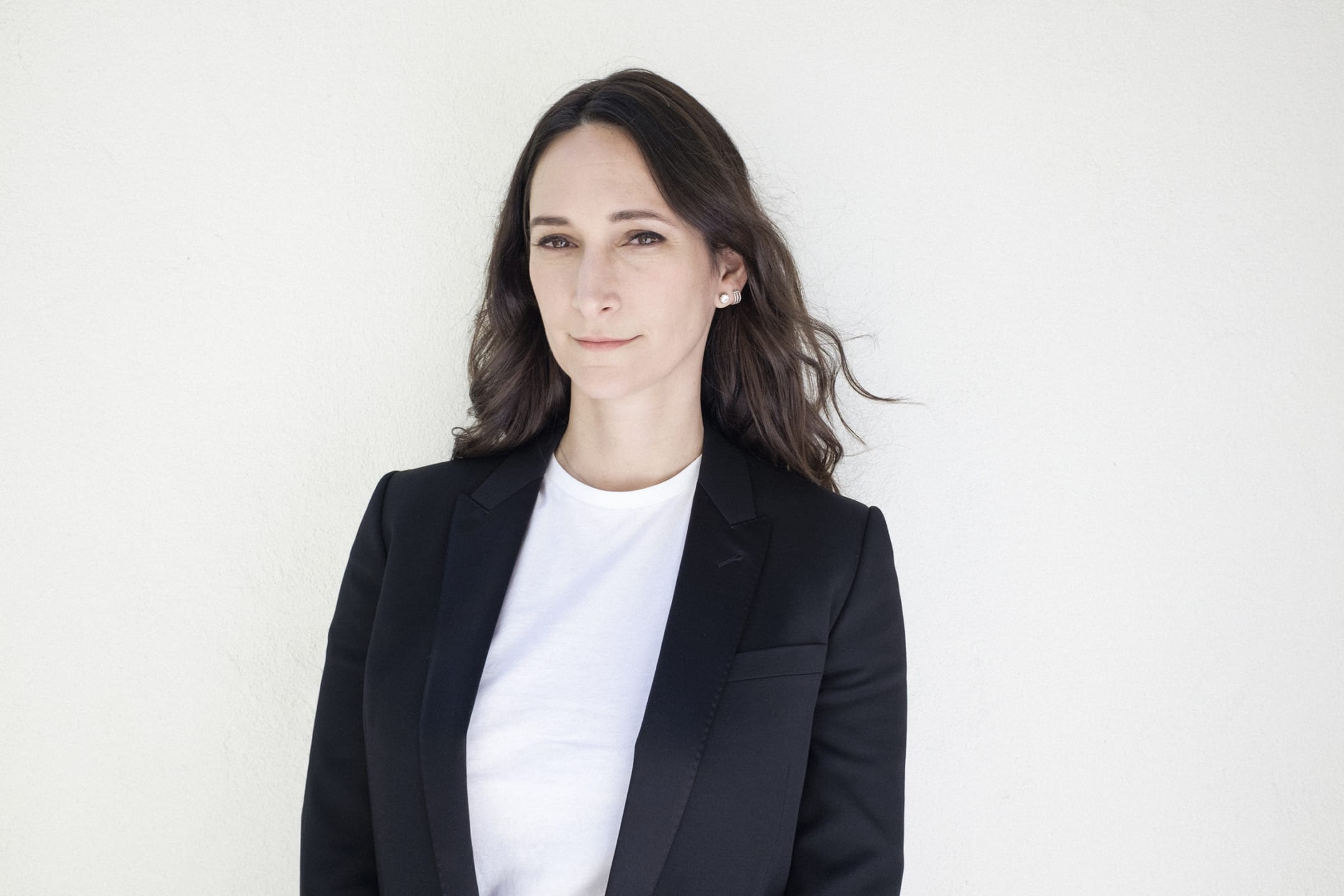 Person in a black blazer and white shirt standing against a light background.