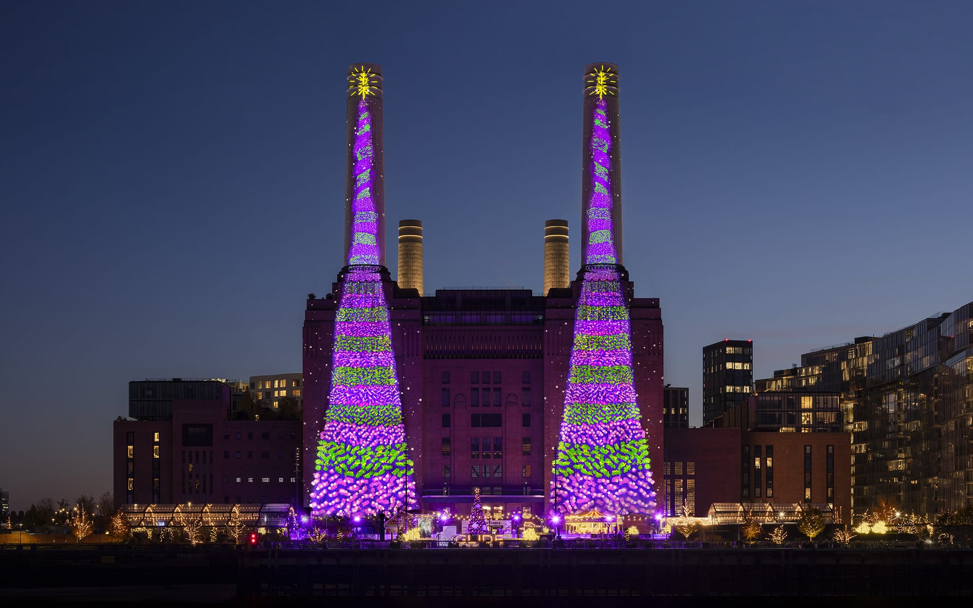 Battersea Power Station illuminated with vibrant purple and green lights during an evening event.