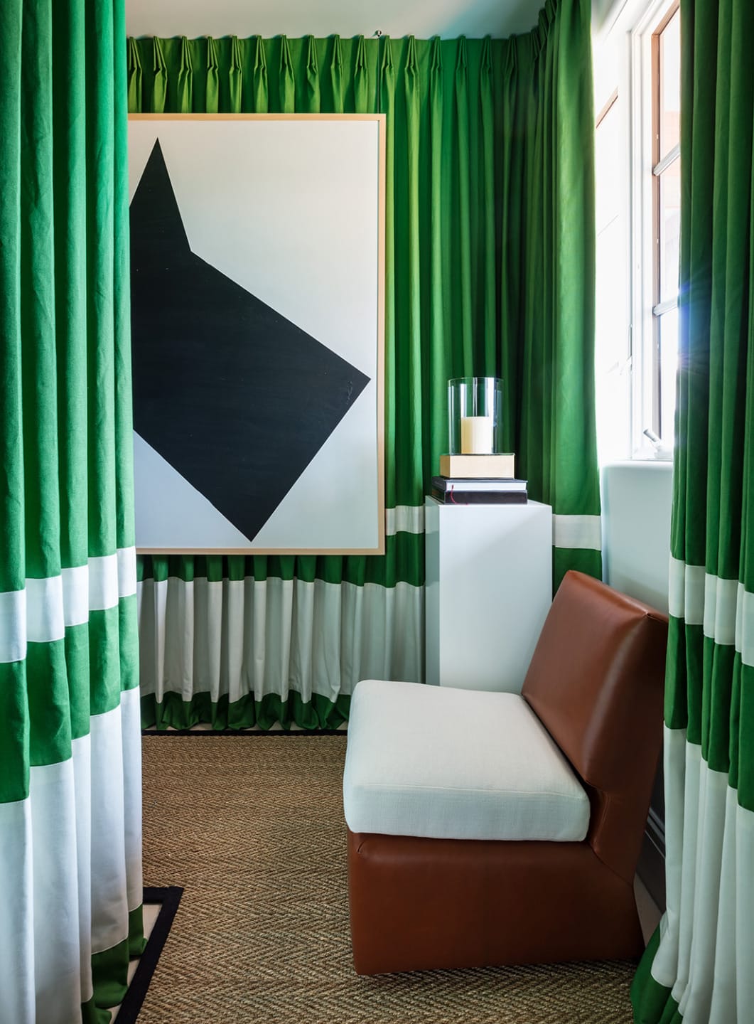 Room with green curtains, abstract art, white pedestal, leather chair, and natural fiber carpet.