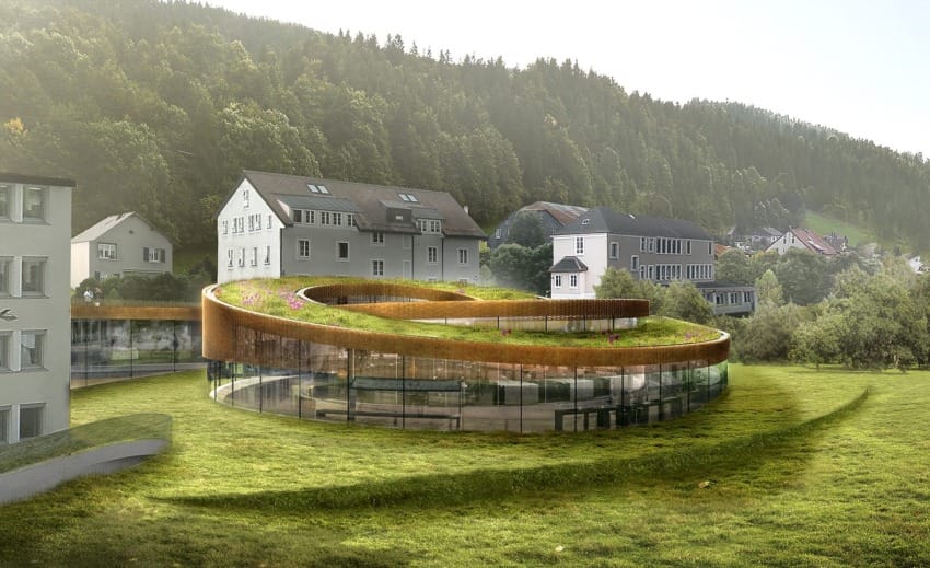 Curved green-roofed building with glass walls surrounded by grass and trees with residential houses in the background