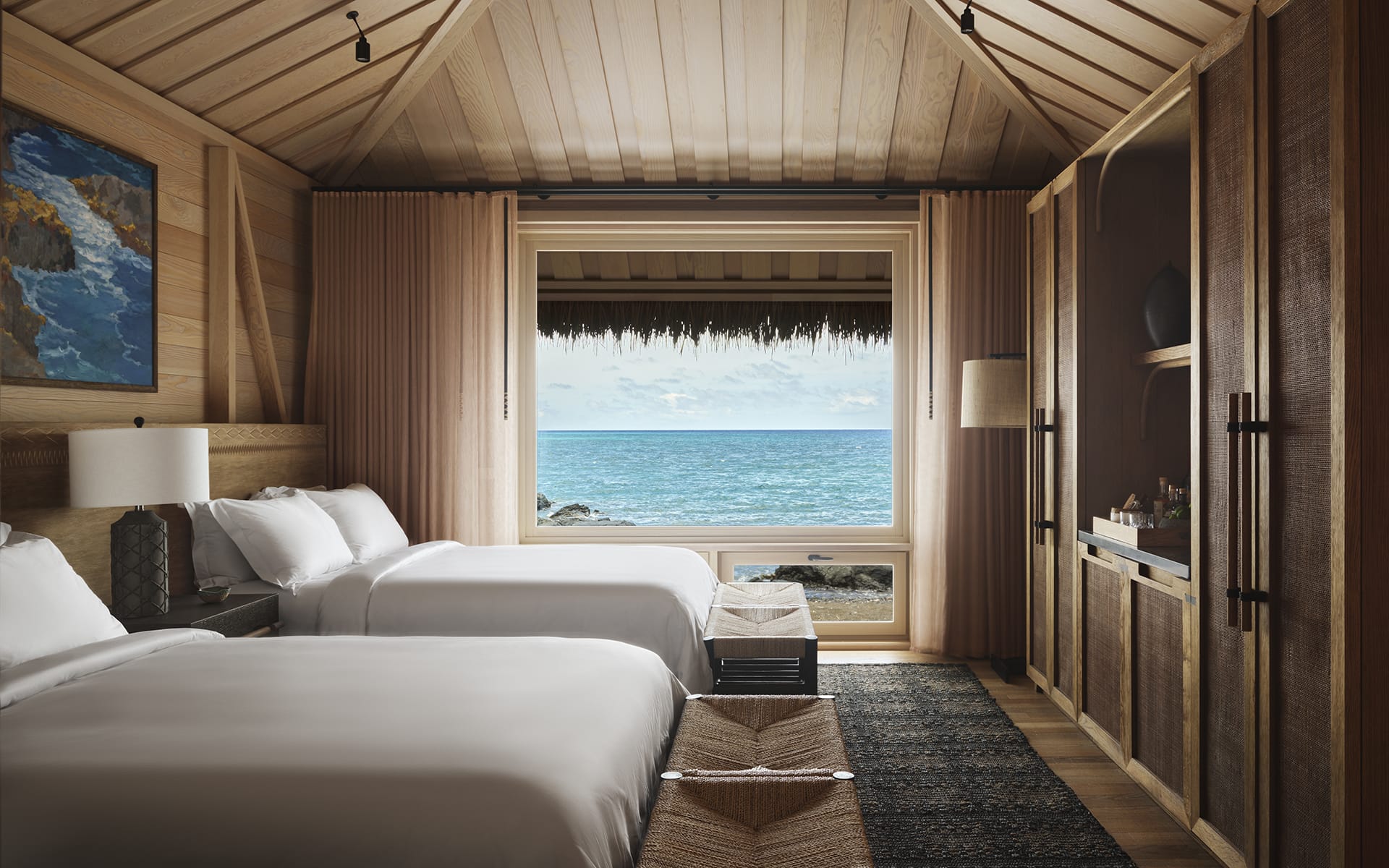 Luxury beachfront room with twin beds, wooden decor, large window view of ocean, and modern amenities.