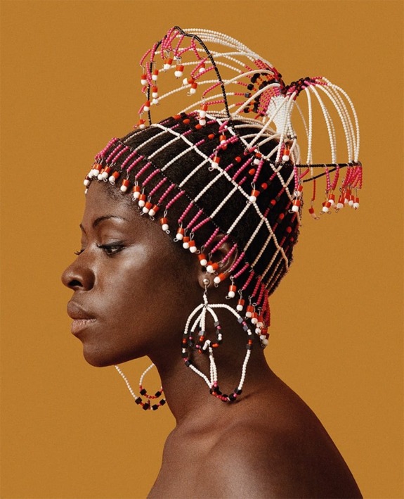 Person with intricate, colorful beaded headpiece and earrings against a solid orange background.