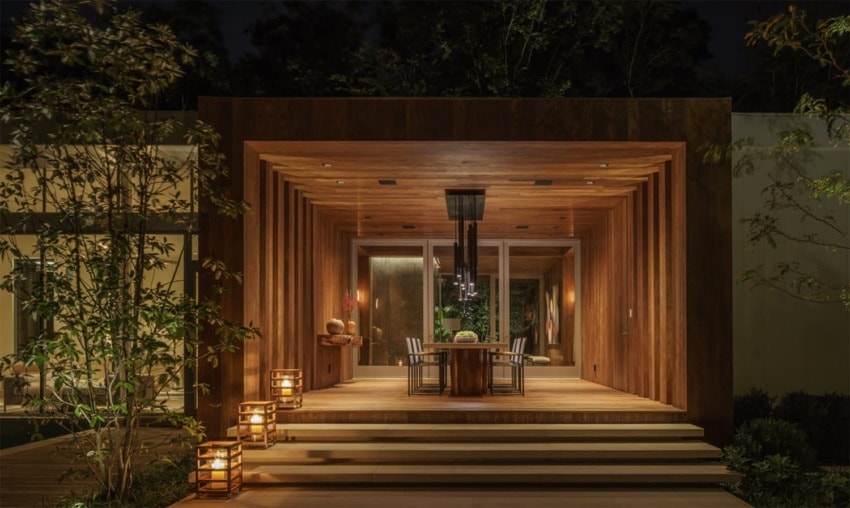 Modern wooden patio at night with ambient lighting and a dining table set for an outdoor gathering.