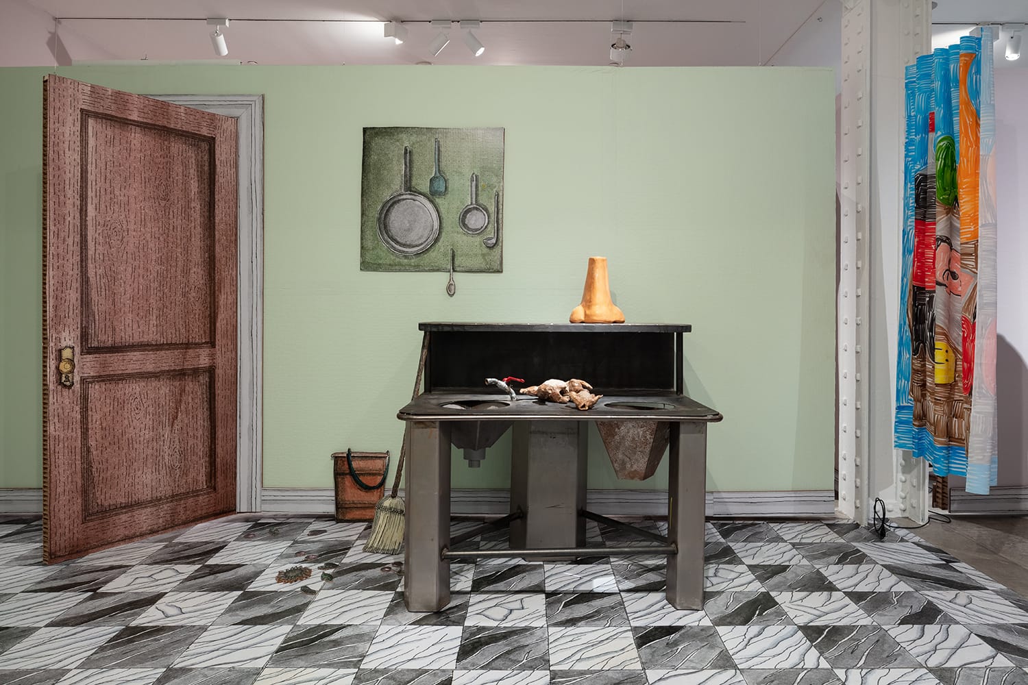 Art installation depicting a surreal kitchen scene with a door, pots on a wall, and a table with objects on a patterned floor.